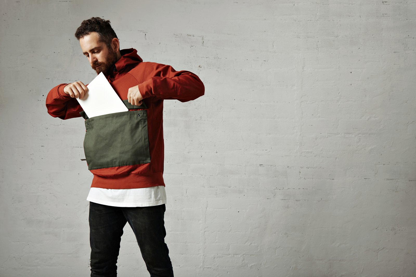 hip-bearded-young-man-putting-blank-sheet-paper-into-huge-front-pocket-his-red-gray-anorak-white-wall (1)